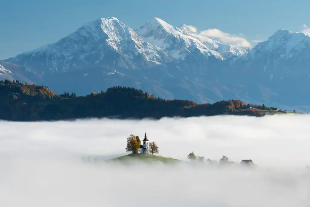 St Thomas Church peeking out of the dense fog layer with Slovenian Alps in the background
